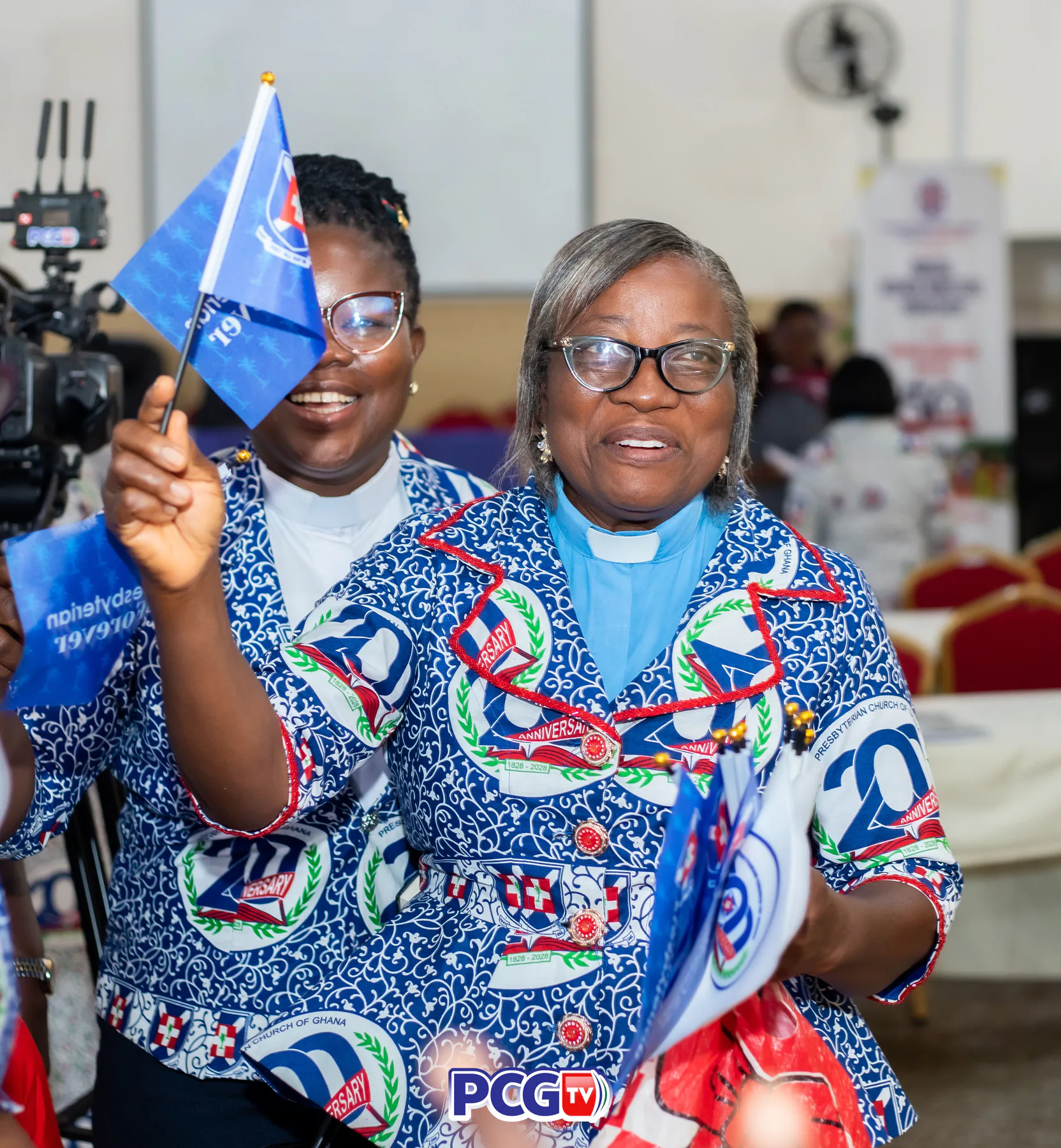 Two Presbyterian women holding anniversary flags and smiling